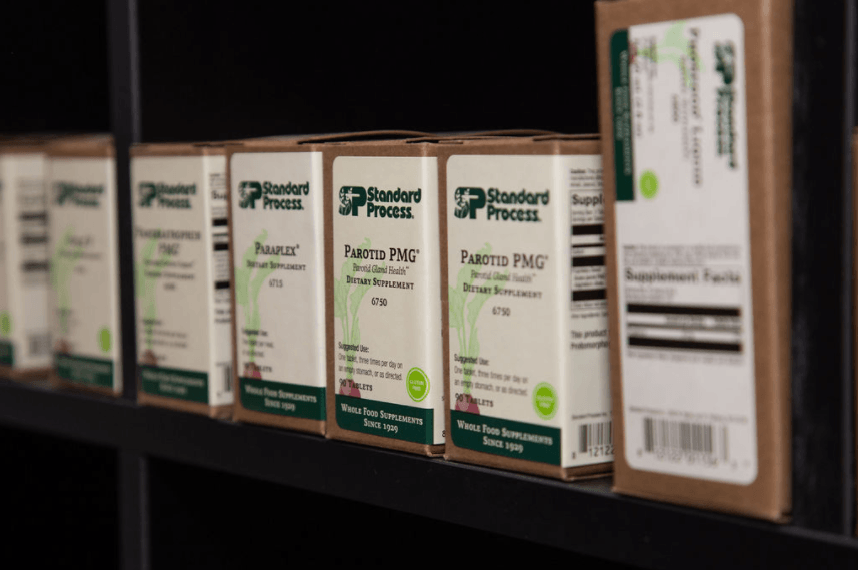Boxes of Standard Process supplements on a shelf, labeled with product names and ingredient information.