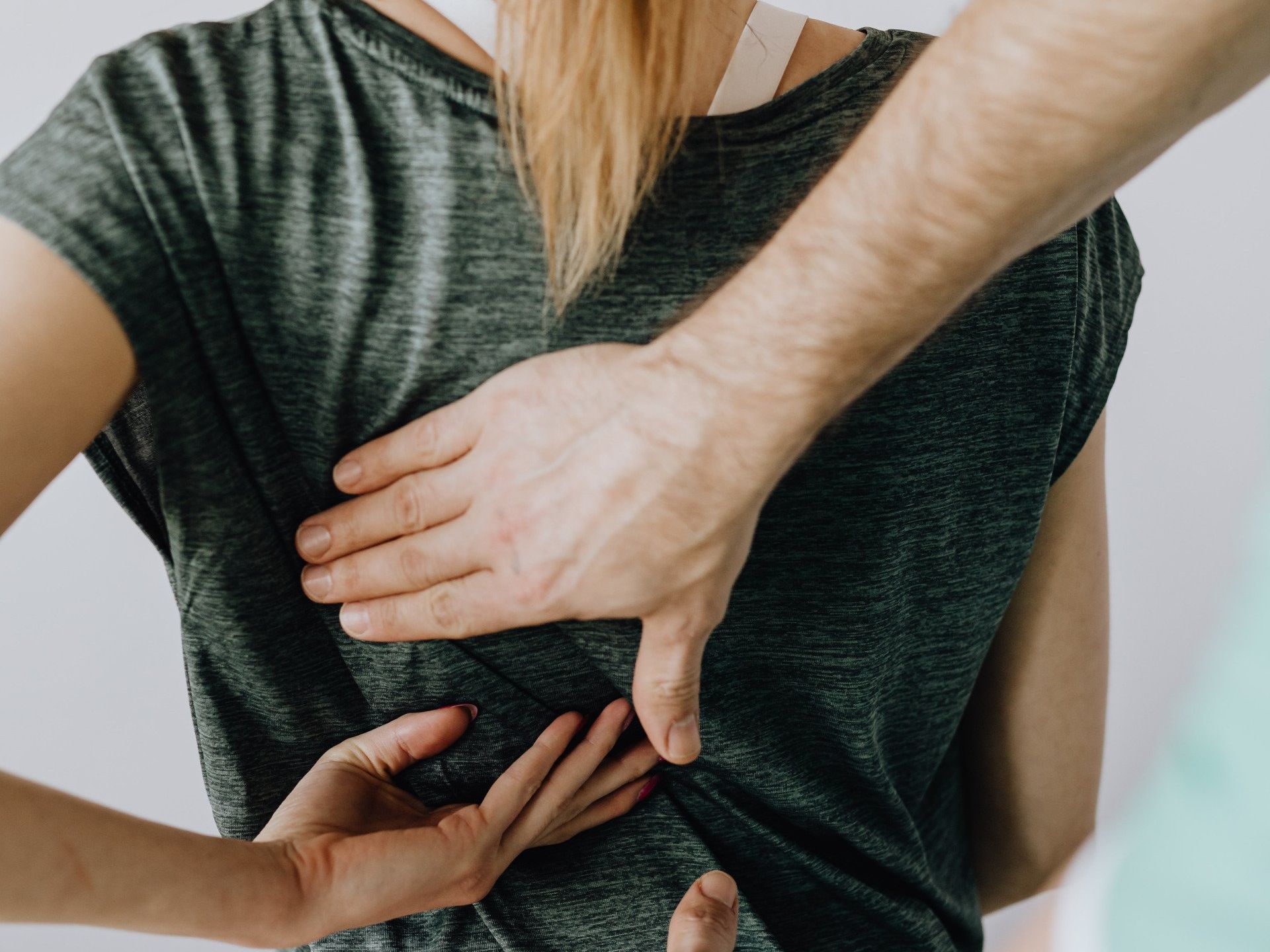Hands on a person's lower back, possibly for a medical exam or massage, person wearing a gray shirt.