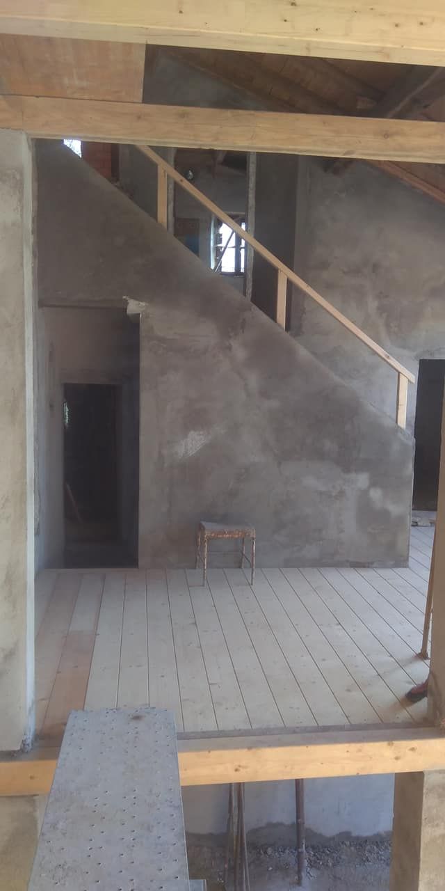 Interno vuoto e non rifinito con pavimento piastrellato, travi a vista e parete della scala in costruzione.