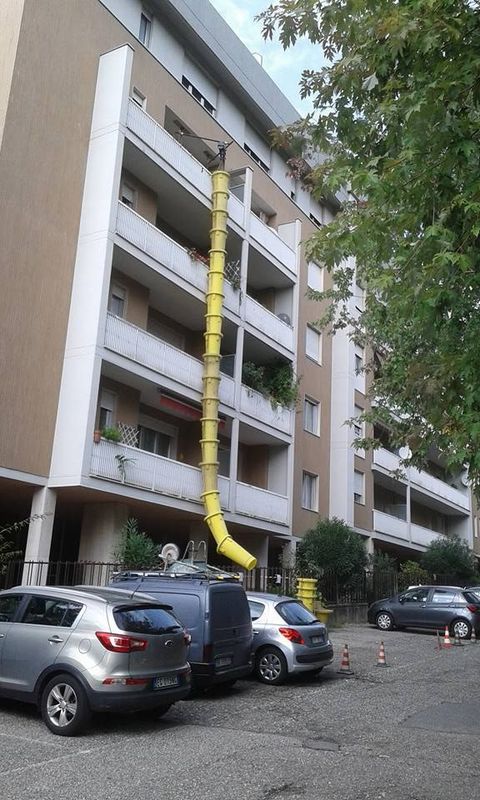 Condominio con un tubo flessibile giallo che scende dai piani superiori verso le auto parcheggiate sottostanti.