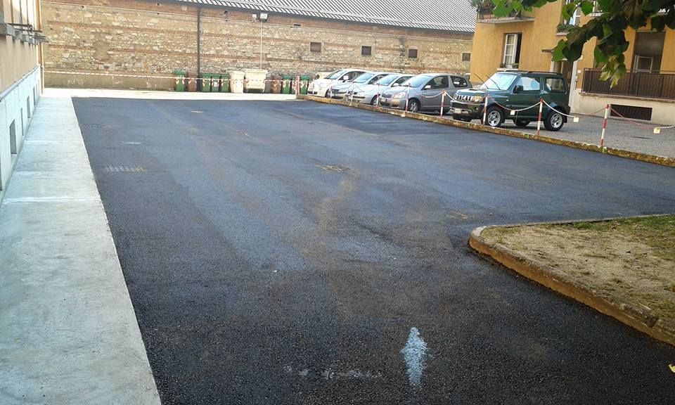 Parcheggio asfaltato vuoto accanto a una fila di auto parcheggiate e al muro di un edificio.