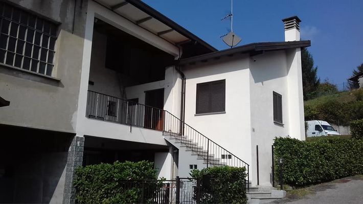 Casa bianca con scala esterna e balcone accanto a un edificio grigio in una giornata di sole