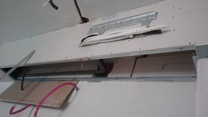 Pannello elettrico a muro aperto con fili a vista e un cavo rosa penzolante