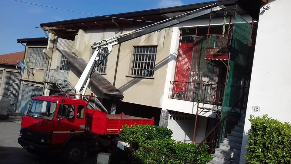 Un camion con gru rosso solleva o sostiene il tetto di una casa a due piani danneggiata.