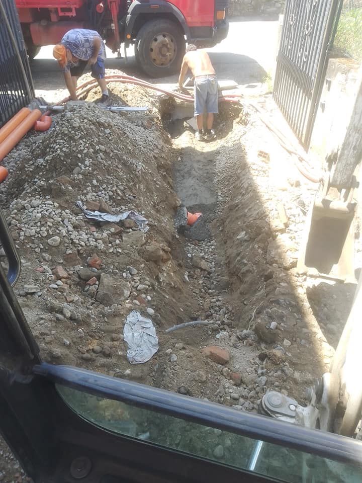 Operai che scavano una trincea accanto a un camion rosso in una stretta area di cantiere.