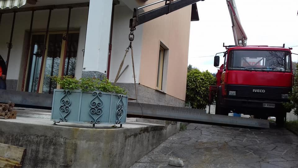Un camion rosso solleva una lunga lastra di cemento accanto al vialetto di una casa.