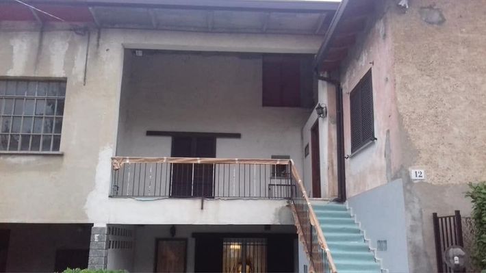 Casa a due piani dall'aspetto vissuto, con balcone e scala esterna color verde acqua che conduce all'ingresso superiore.