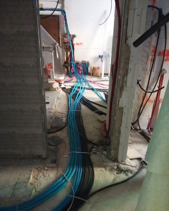 Cavi blu che attraversano uno stretto corridoio di cantiere con pareti grezze e blocchi di cemento.