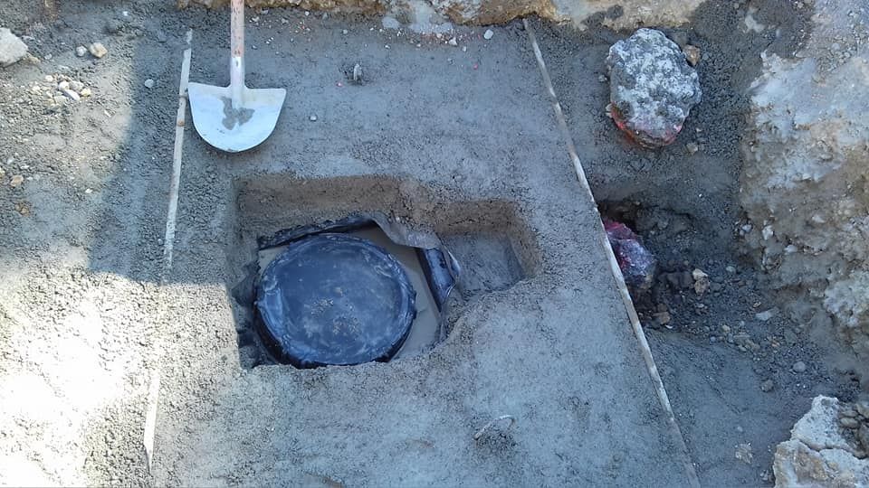 Terreno scavato con un oggetto rotondo sepolto in una fossa quadrata e una pala nelle vicinanze.