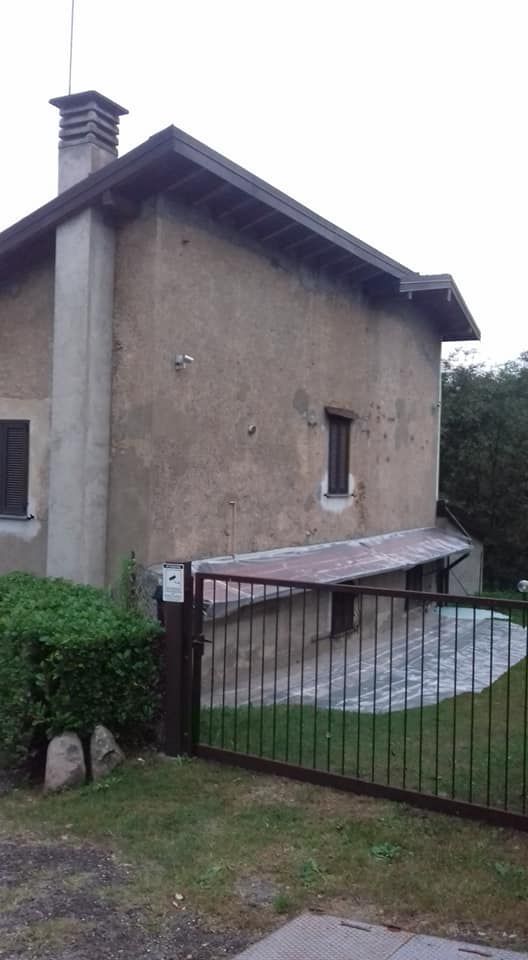 Esterno di una casa in pietra con una piccola finestra, tetto spiovente e cancello in metallo in un cortile erboso.