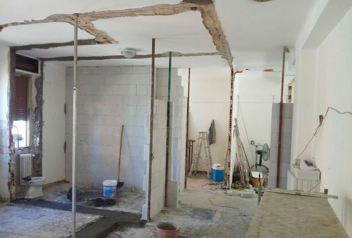 Stanza parzialmente demolita con travi del soffitto a vista, detriti e attrezzi da costruzione durante i lavori di ristrutturazione.
