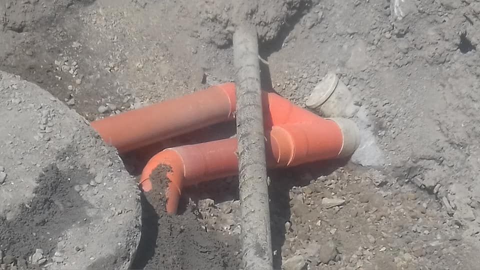 Tubi arancioni e un'asta nera giacciono in una trincea di terra tra rocce e detriti.