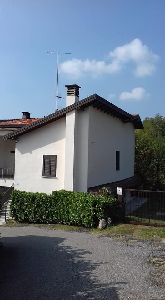Piccola casa bianca con il tetto di tegole rosse, accanto a una strada, sotto un cielo azzurro con nuvole.