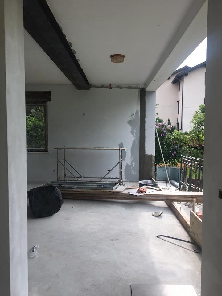 Veranda coperta vuota con pavimento in cemento, materiali edili sparsi e una parete parzialmente dipinta.