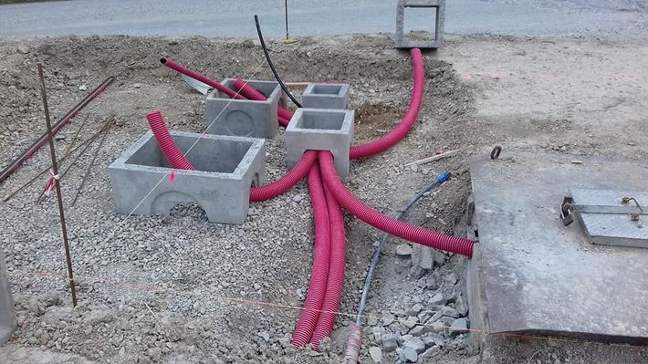 Scatole di cemento per servizi pubblici con tubi rosa acceso che attraversano un cantiere ghiaioso.