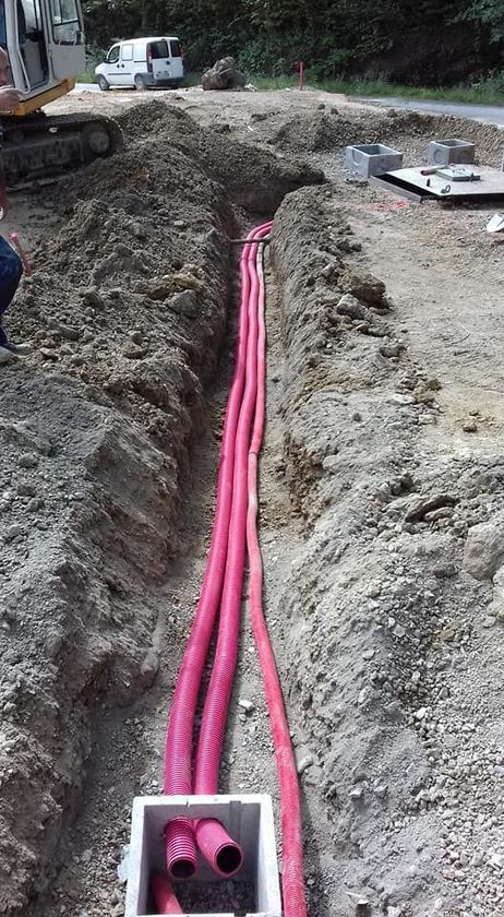 Tubature di servizio rosa in una trincea in un cantiere, con un escavatore nelle vicinanze.