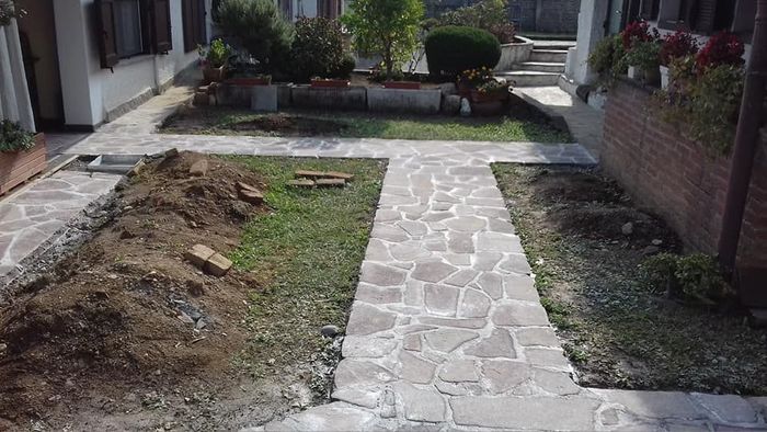 Sentiero in pietra tra gli edifici residenziali, con terra smossa sul lato sinistro.