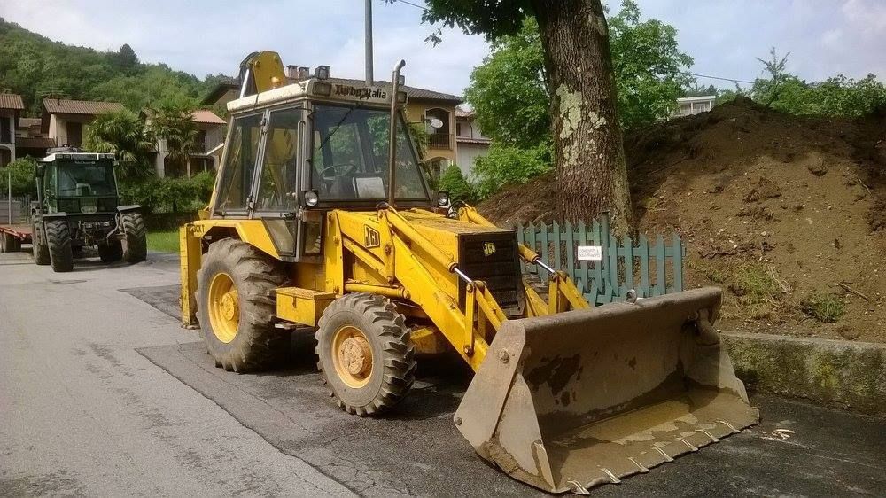 Una terna gialla parcheggiata in una strada residenziale accanto a un albero e a una recinzione.