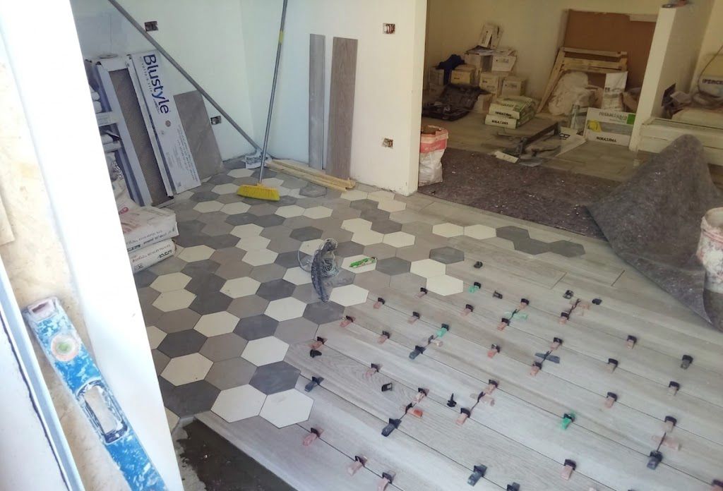 Stanza ristrutturata con nuovo pavimento in piastrelle decorate, attrezzi e materiali edili sparsi ovunque.