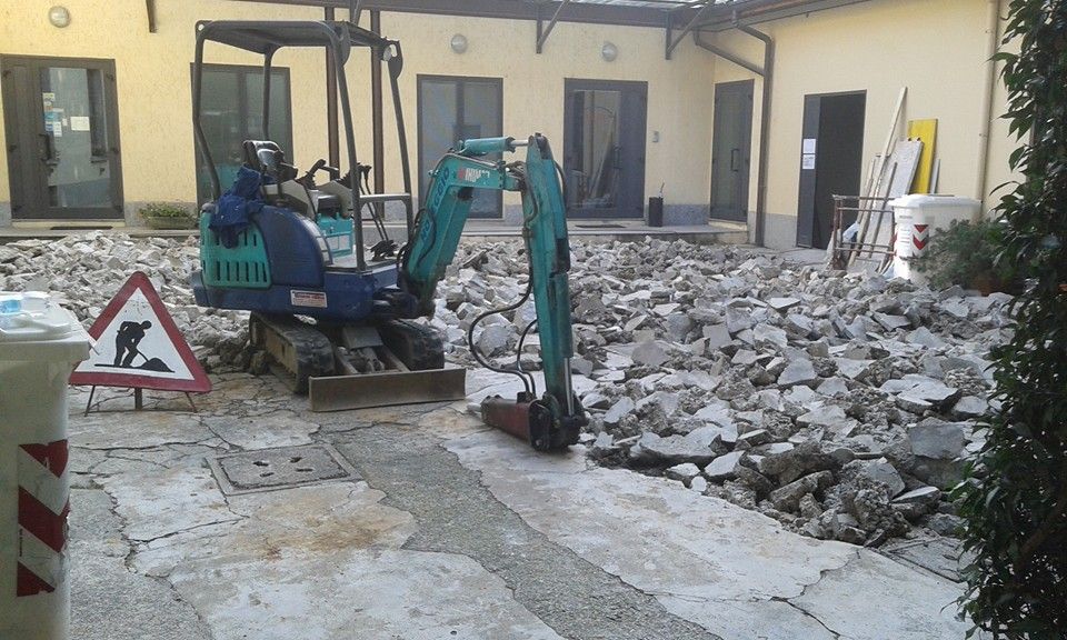 Un miniescavatore rimuove un cumulo di macerie in un cortile adiacente a un edificio in ristrutturazione.