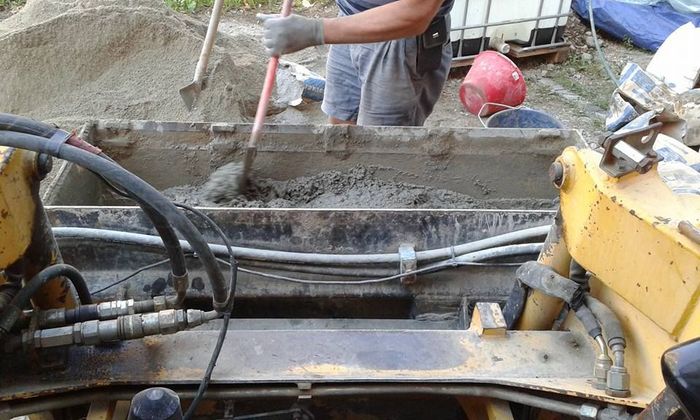 Operaio edile che manovra macchinari con tubi flessibili e calcestruzzo fresco in un cantiere.