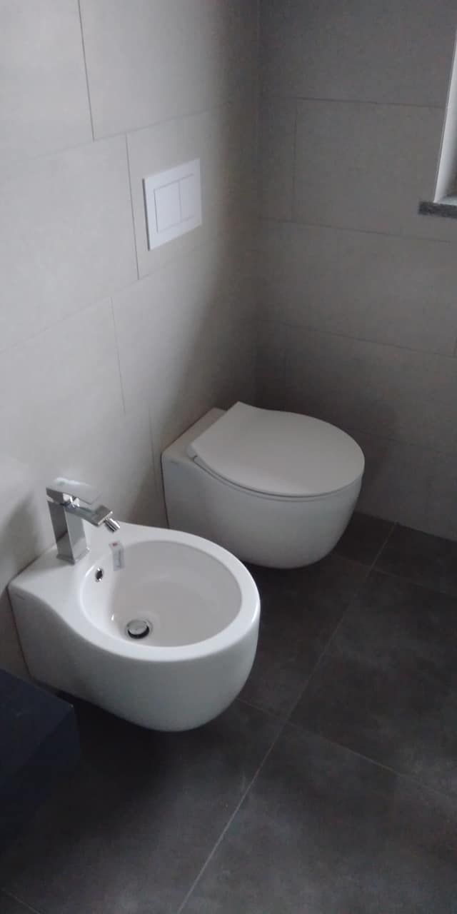 Piccolo bagno grigio con WC sospeso e bidet bianco accanto.