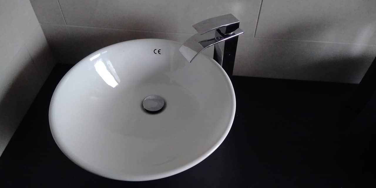 Lavabo in ceramica bianca con rubinetto cromato su un piano di lavoro scuro, contro una parete grigia.
