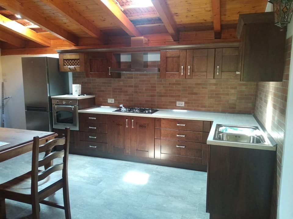 Cucina rustica con mobili in legno, paraschizzi in mattoni e fornelli sotto un soffitto inclinato in legno.