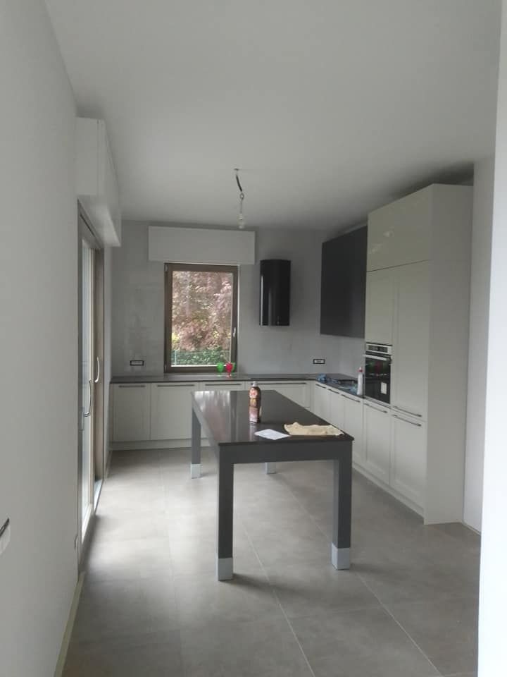 Cucina moderna con mobili bianchi, pavimento in piastrelle grigie e tavolo da pranzo nero vicino a una finestra.