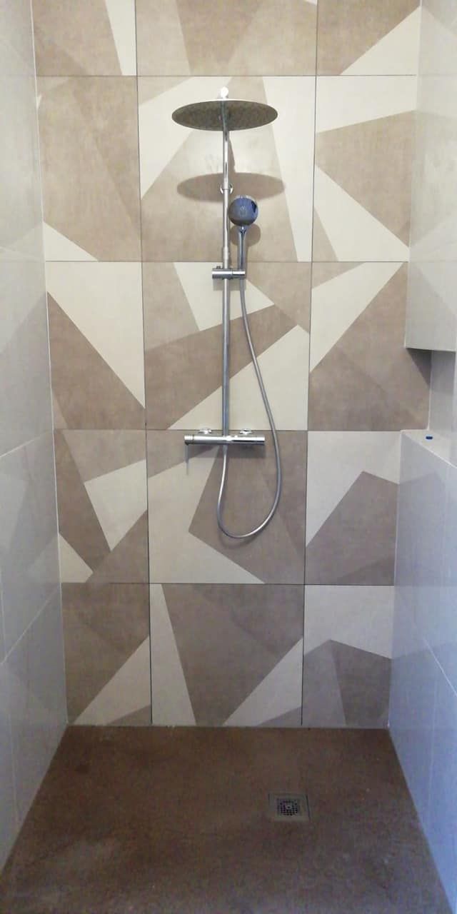 Doccia piastrellata con soffione a parete, flessibile e scarico a pavimento in un bagno.