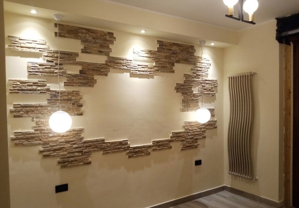 Parete decorativa del soggiorno con inserti in pietra, due lampade rotonde e un radiatore verticale alto.