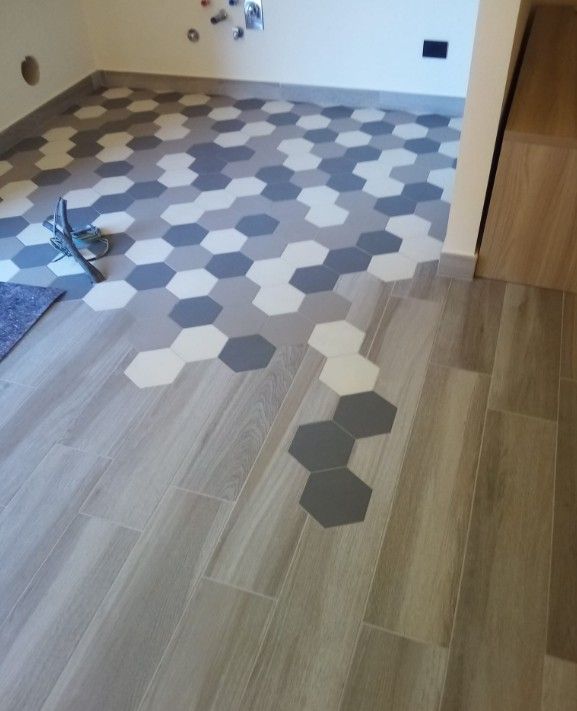 Interno di una stanza con pavimento in piastrelle esagonali miste che sfumano in assi effetto legno.