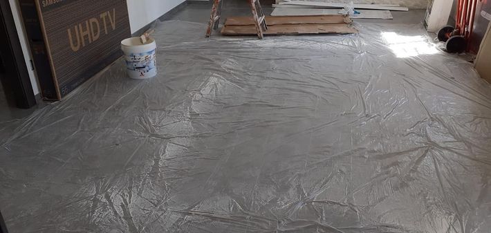 In una stanza interna, si sta lisciando un pavimento in cemento grigio, con un secchio e materiali edili nelle vicinanze.