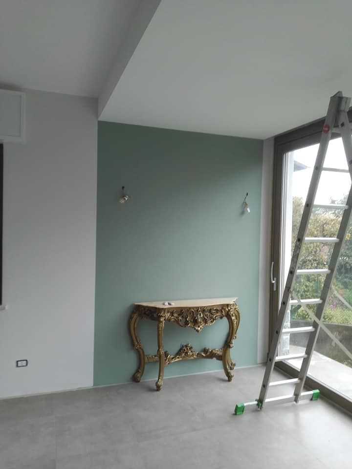 Stanza parzialmente finita con pareti grigie, tavolo decorato e una scala vicino alla finestra.