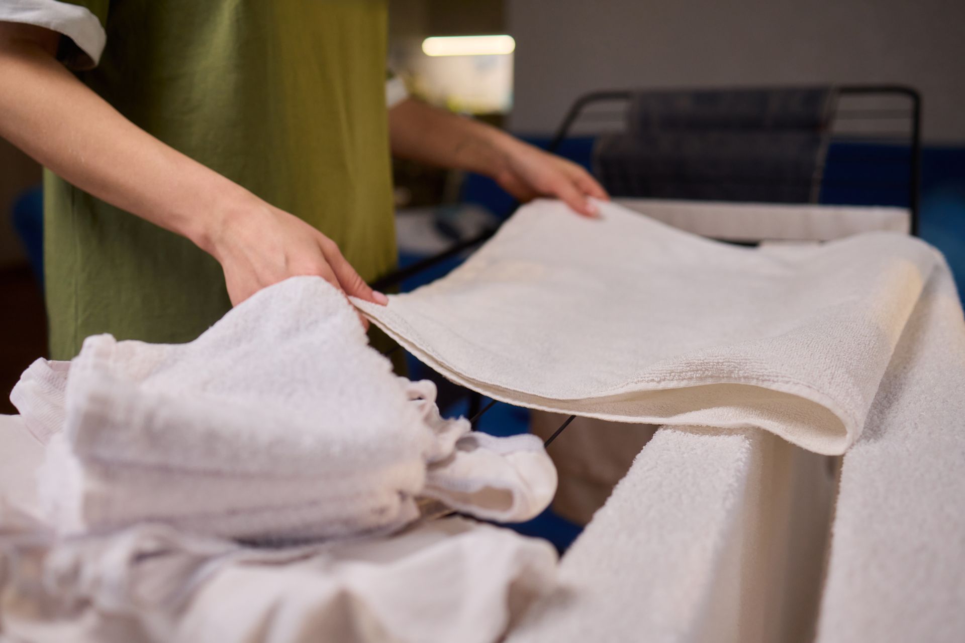 Hands folding white towels on a laundry table with stacked linens in the background
