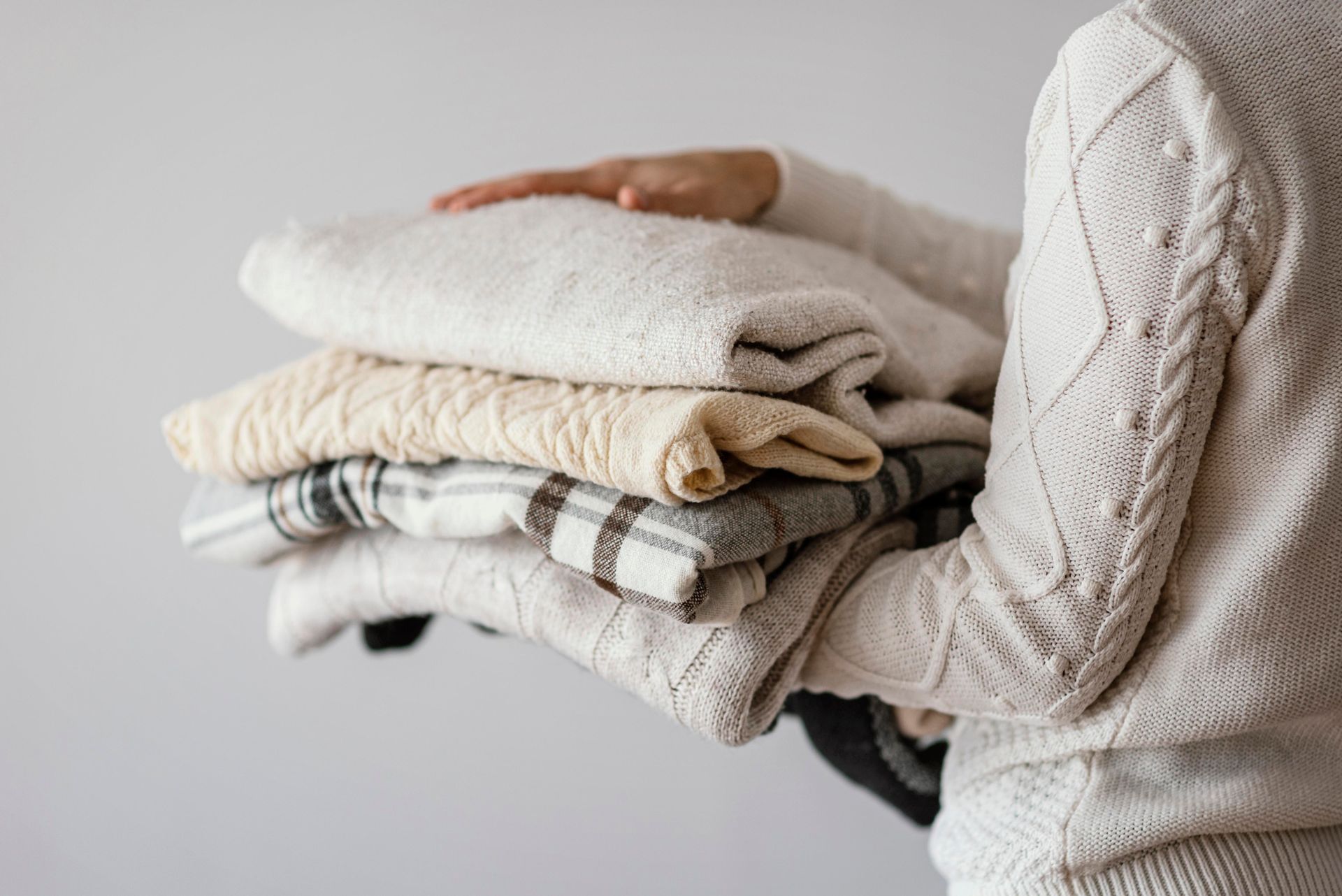 Person holding a stack of folded neutral-colored sweaters and blankets