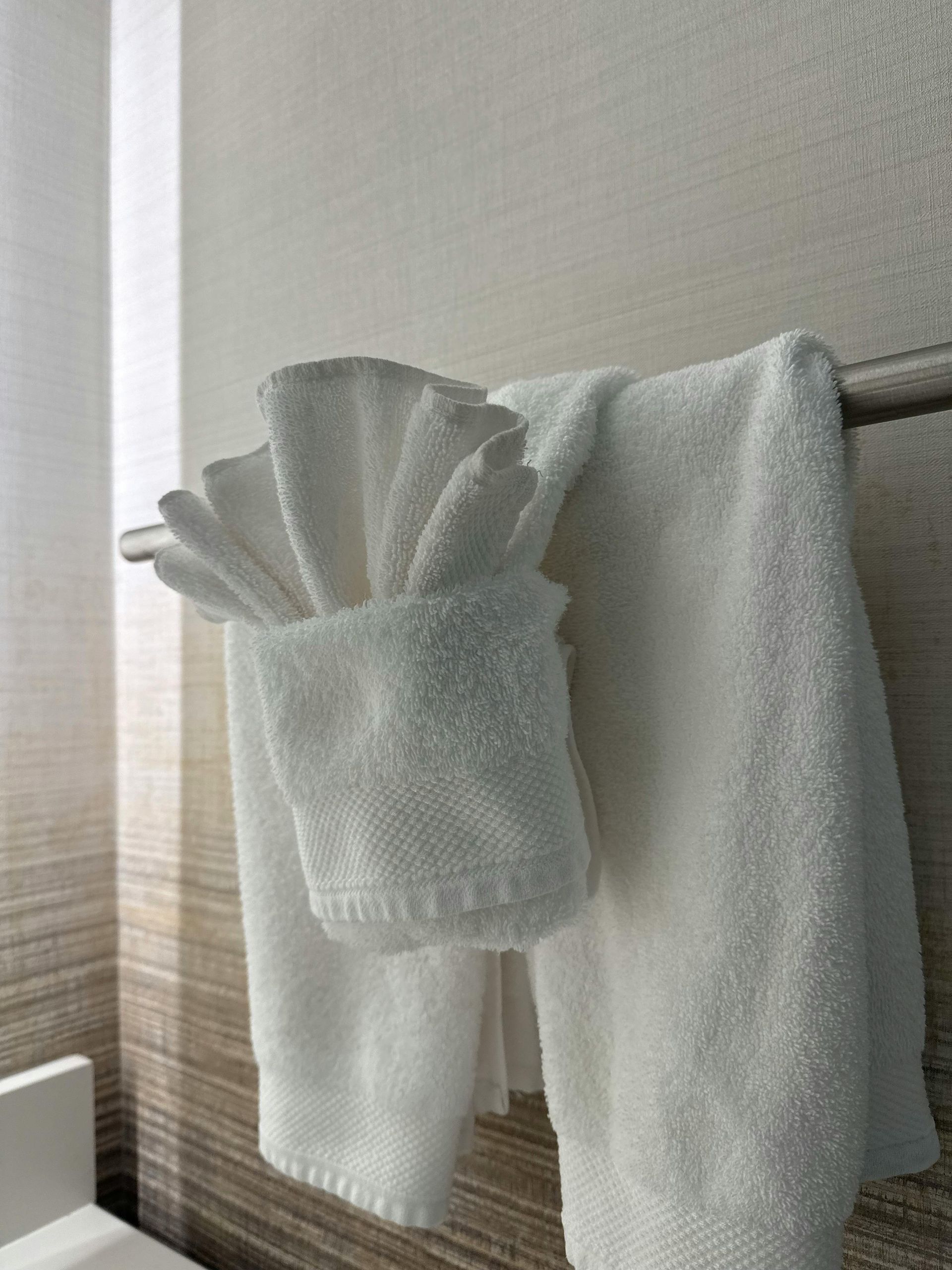 White towel and cloths hanging on a wall hook near a window.