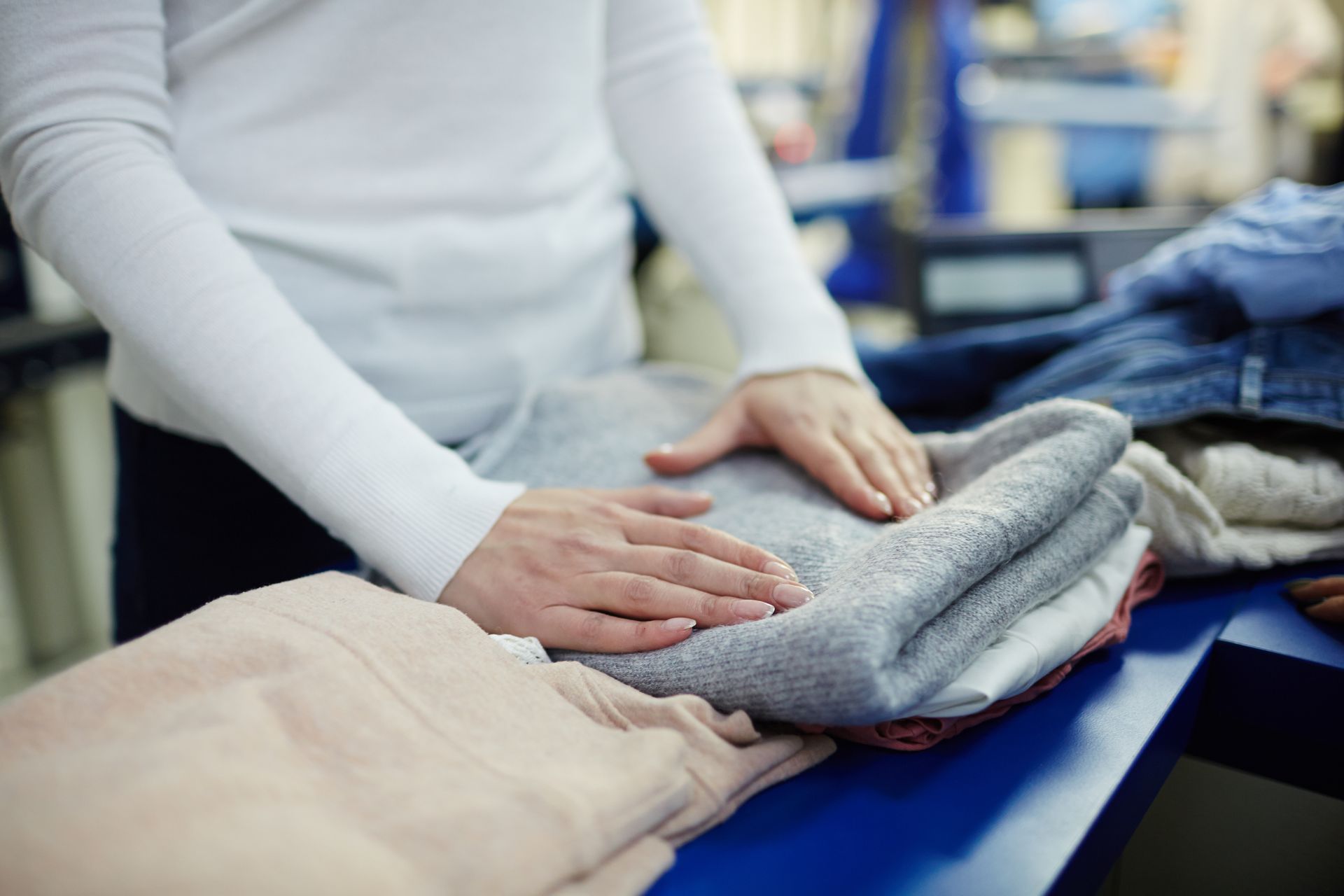 Hands folding clothes on a table in a laundry or retail setting