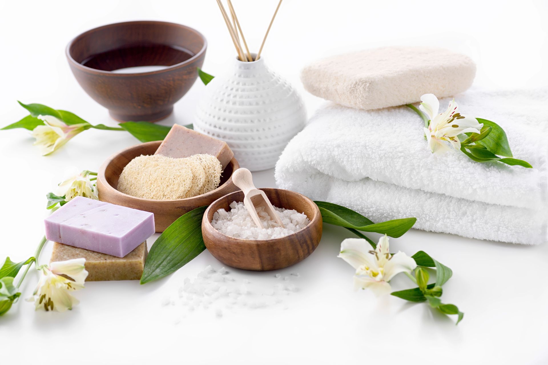 Allestimento da spa: saponi, asciugamani, sali da bagno e fiori disposti su una superficie bianca.