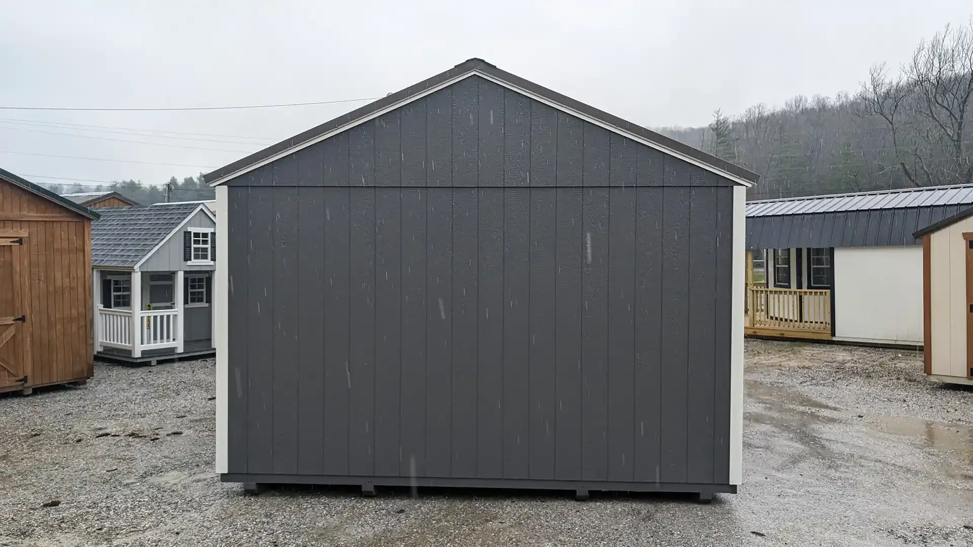 A gray storage shed with white trim sits outside. Other sheds are in the background. It's a rainy day.