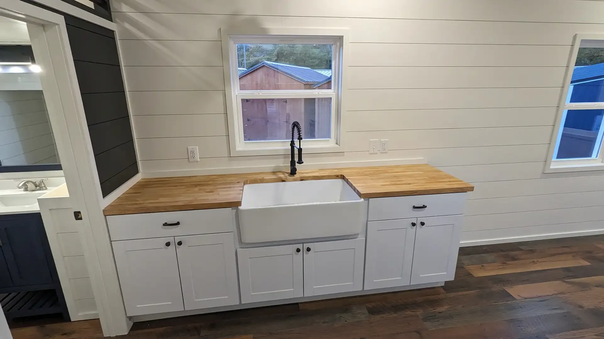 White kitchen cabinets with a wooden countertop, farmhouse sink, and black faucet.
