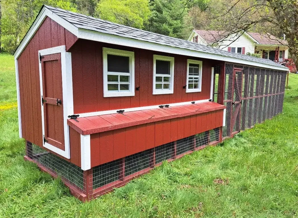 Red chicken coop in a grassy yard, with a connected wire run.