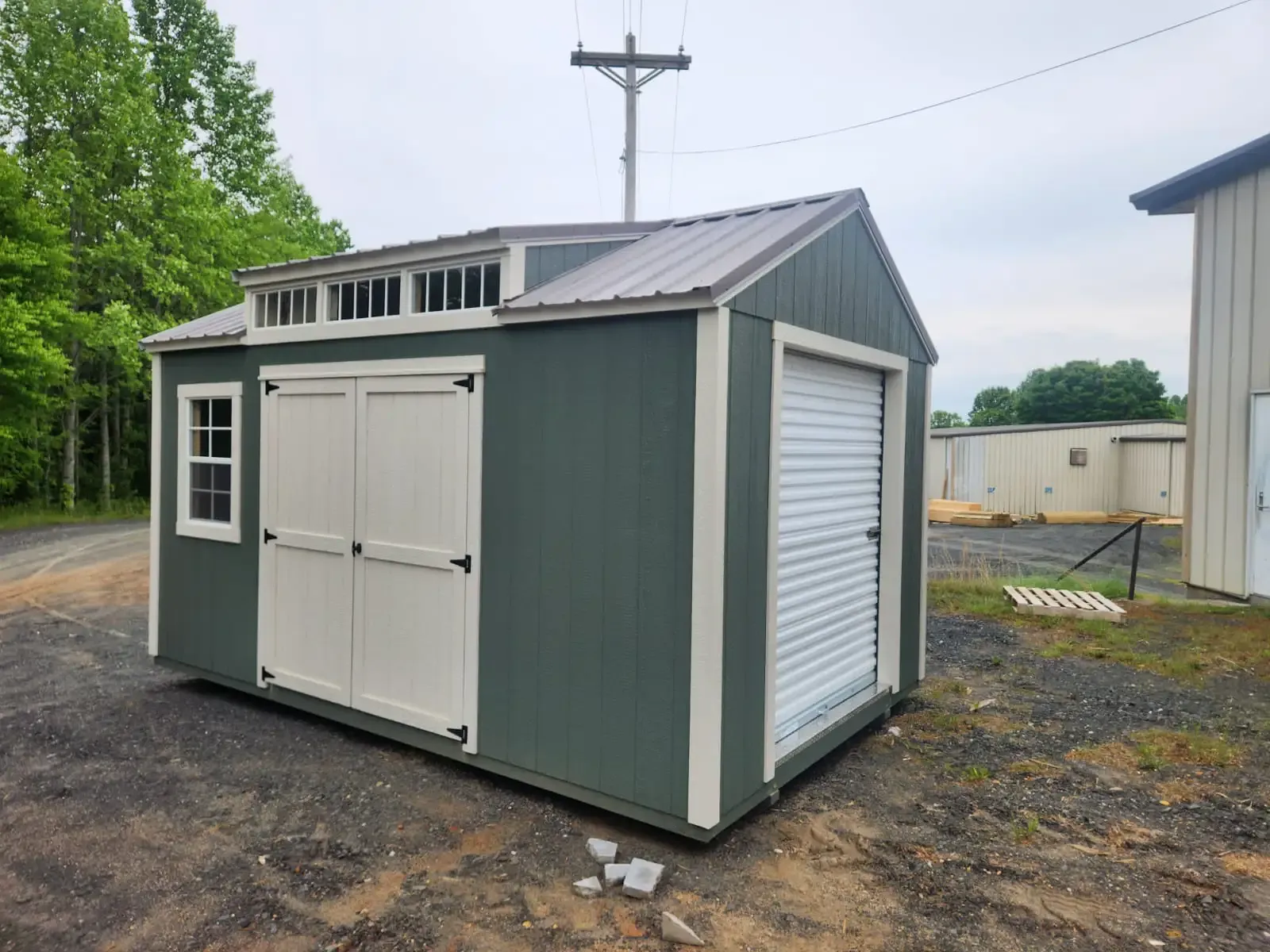 Green and white storage shed with a roll-up door and double doors, set on gravel.