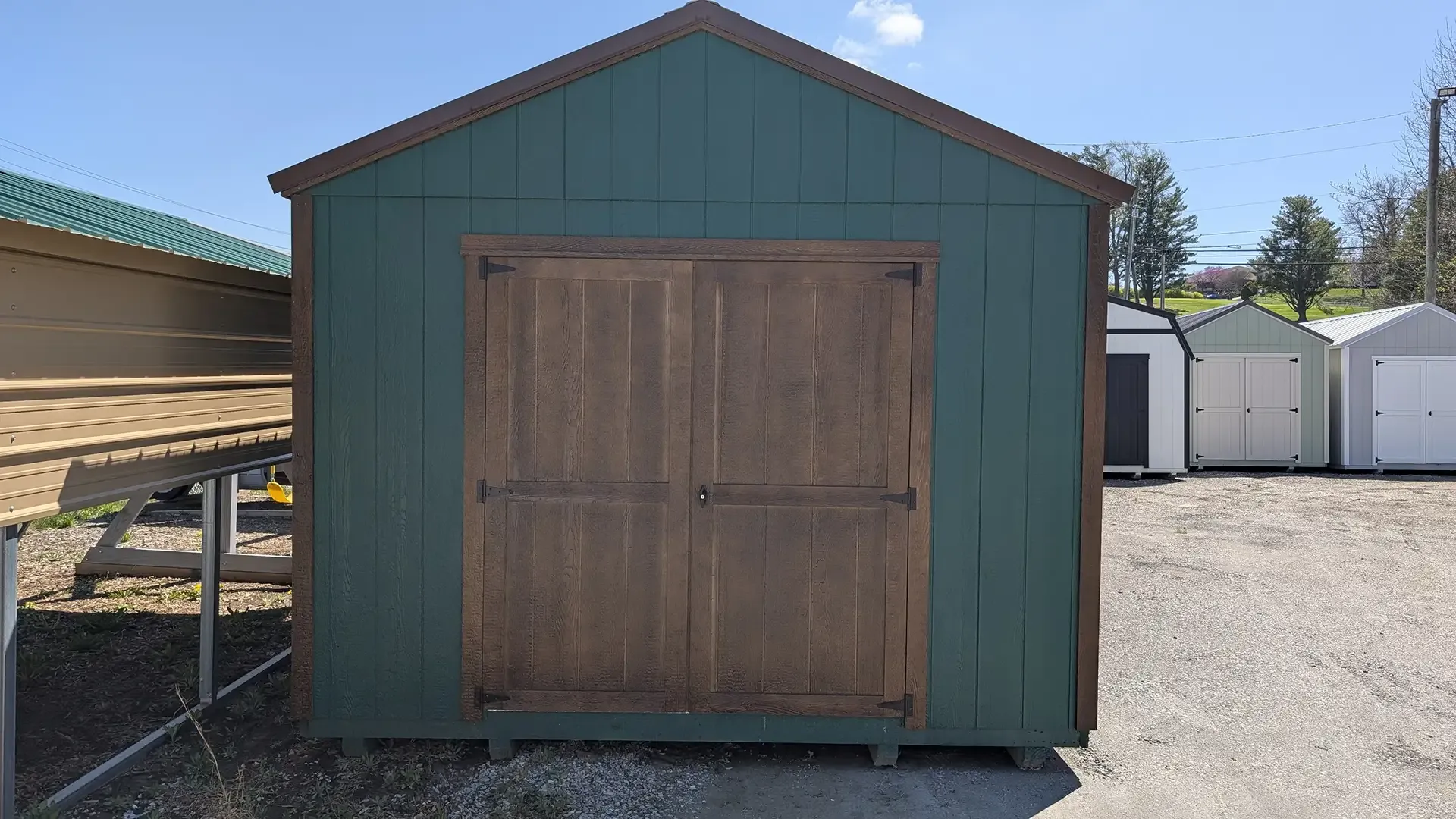 Green shed with brown doors and trim, parked outside on a sunny day.