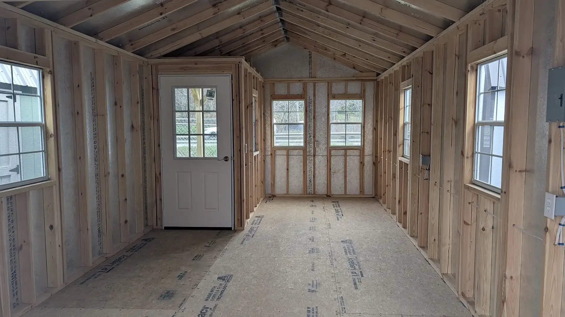 Interior of an unfinished wooden shed with a door, windows, and exposed framing.