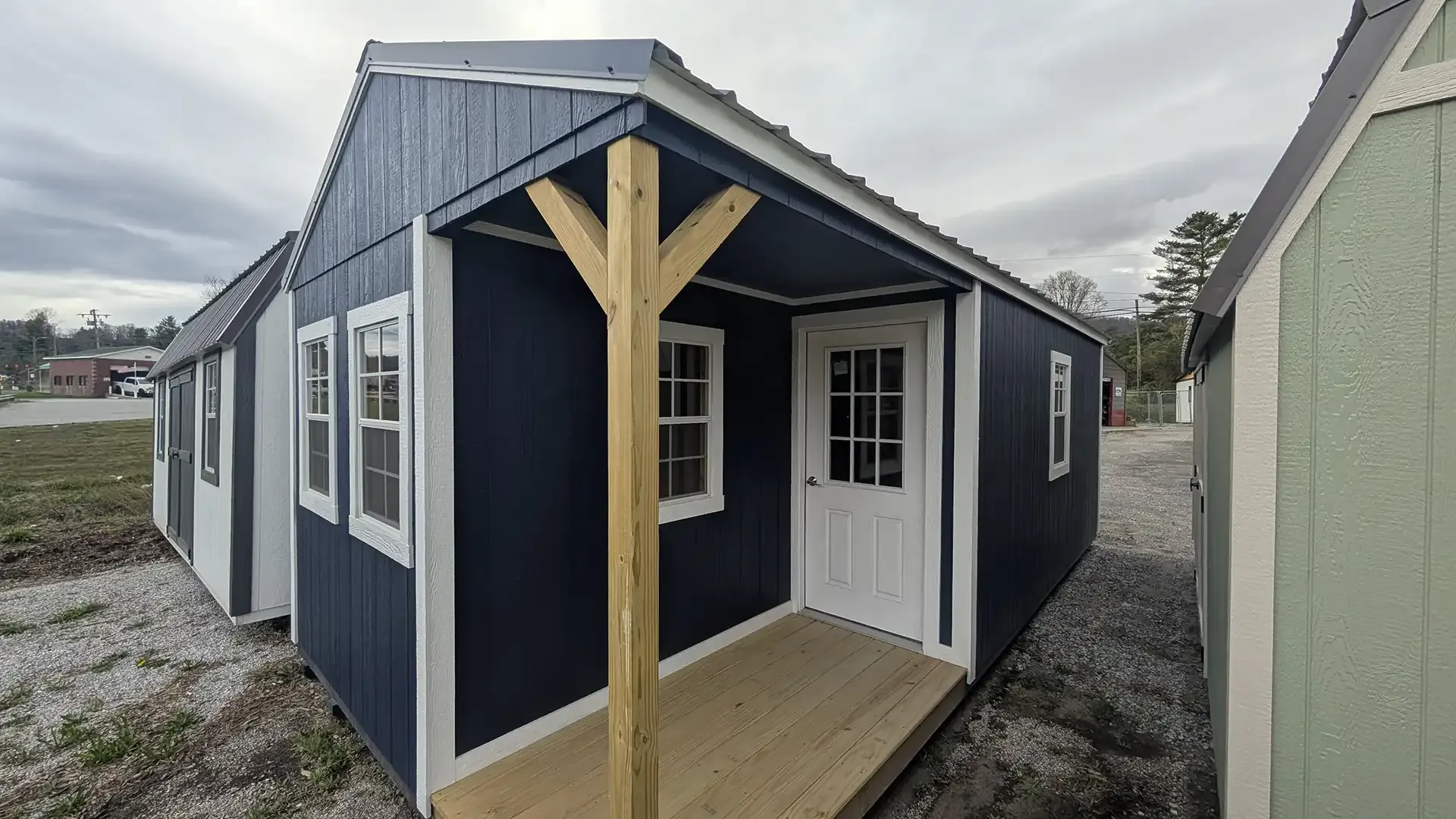 Dark blue cabin with white trim, small porch, and white door. Gray and green cabins in background.