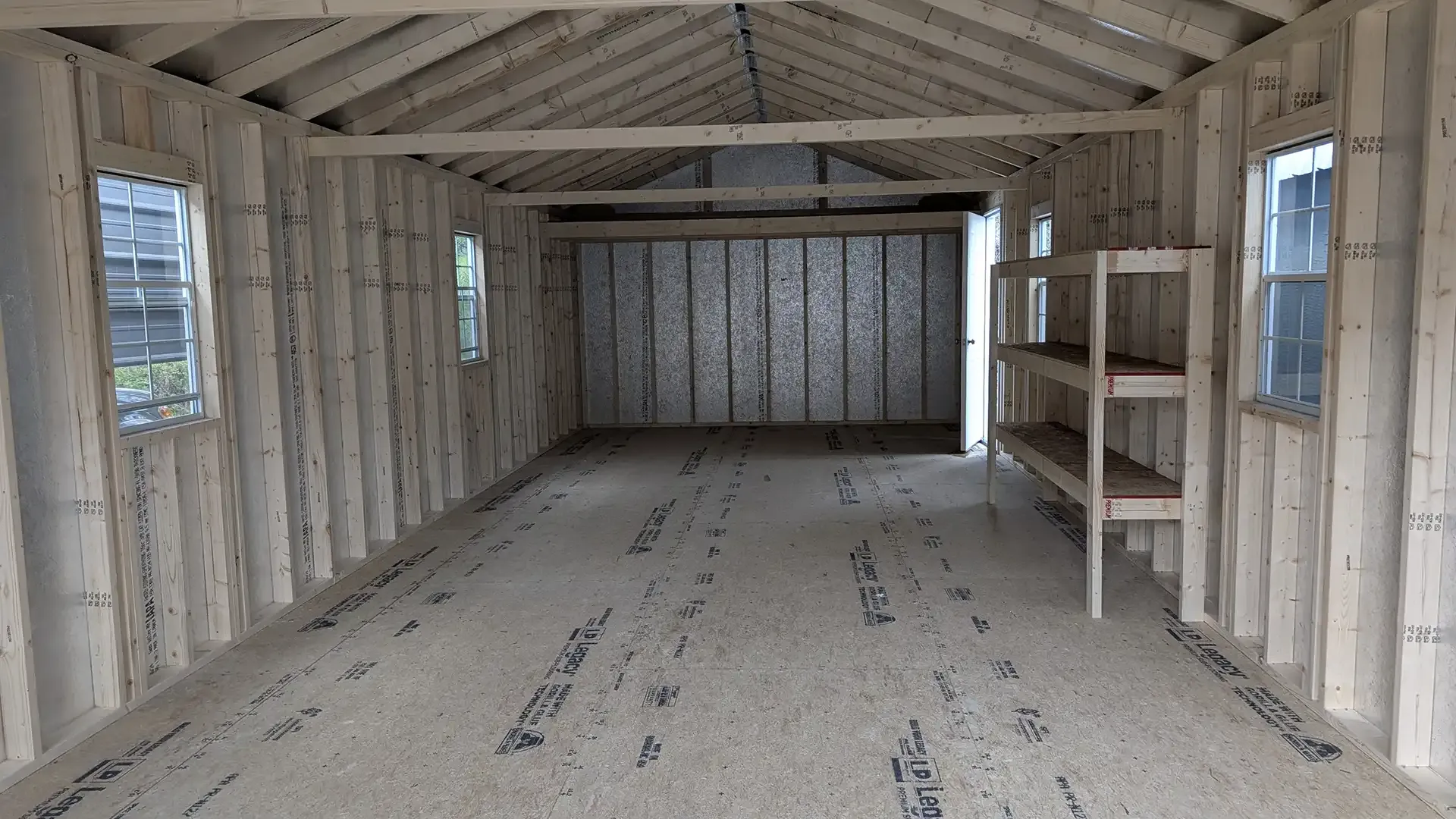 Interior view of a wooden shed with shelves and windows; natural light.