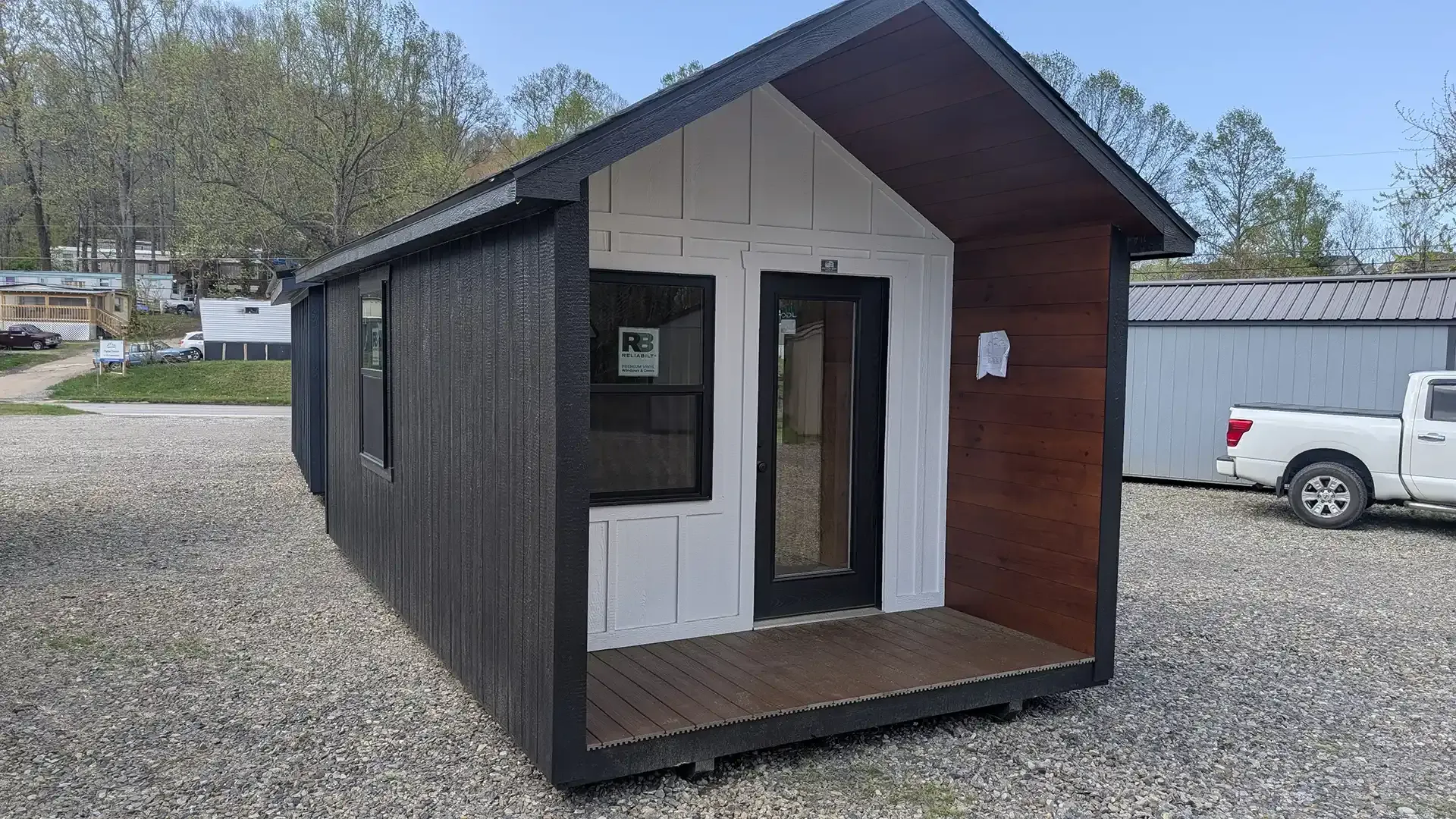 Small, black and white cabin with brown trim, parked outside with a white truck.