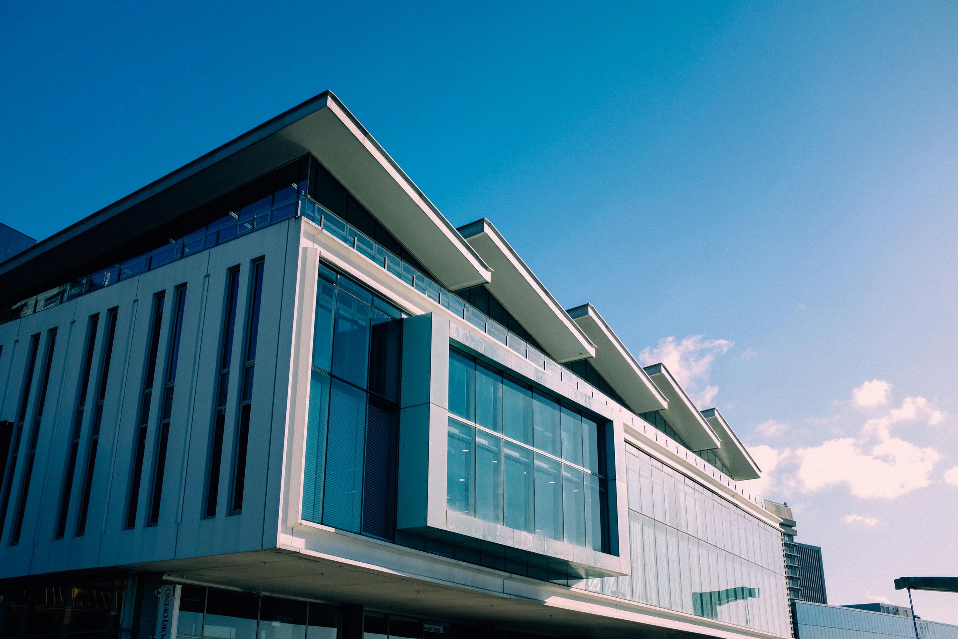 Modern building with a zigzag roof and large windows against a bright blue sky.