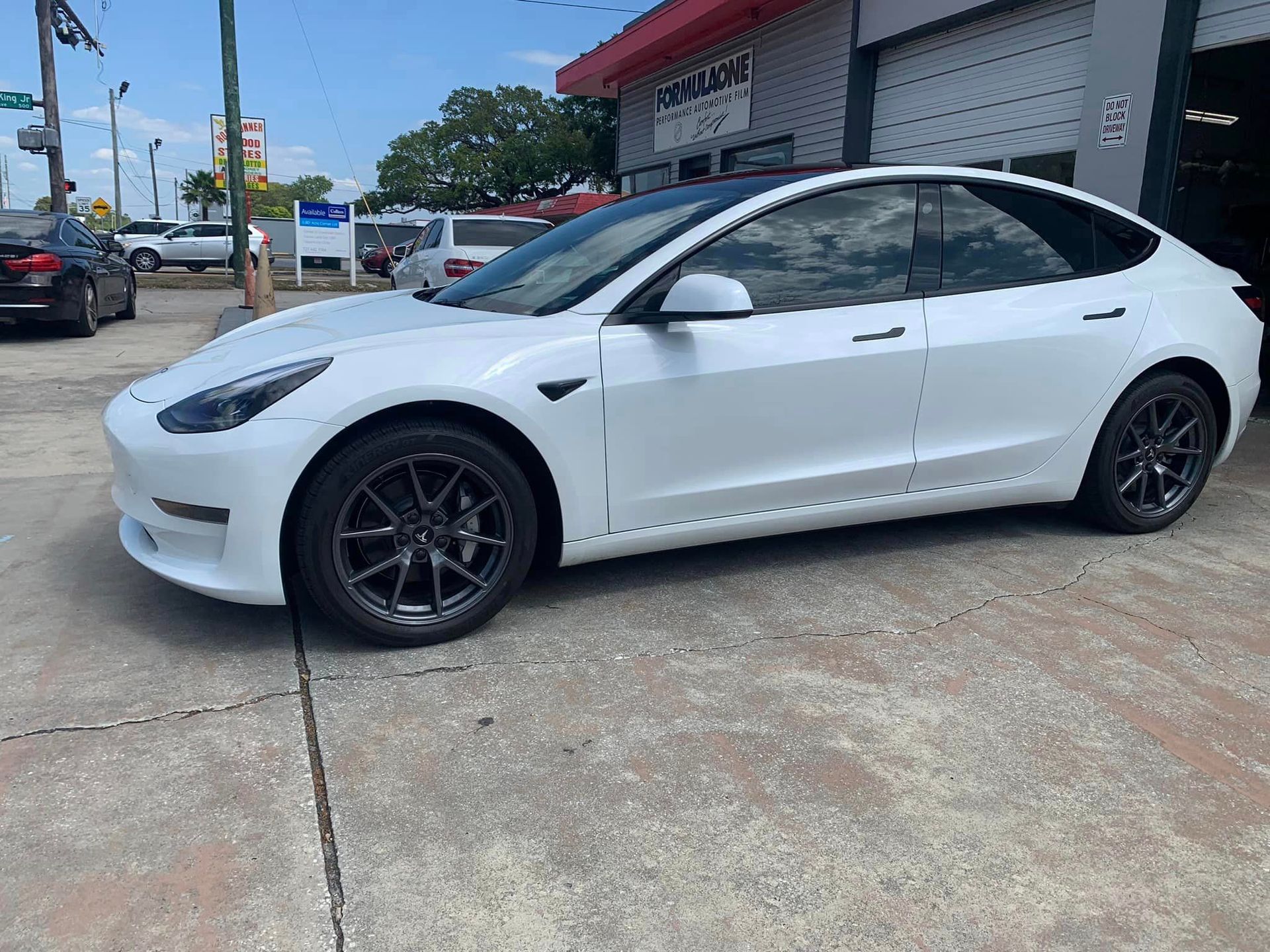 White Tesla sedan parked outside a storefront on a concrete lot